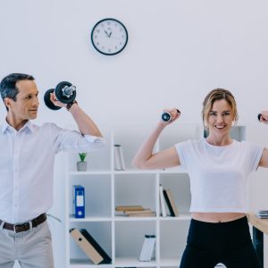 happy mature businessman with his personal trainer working out with dumbbells at office
