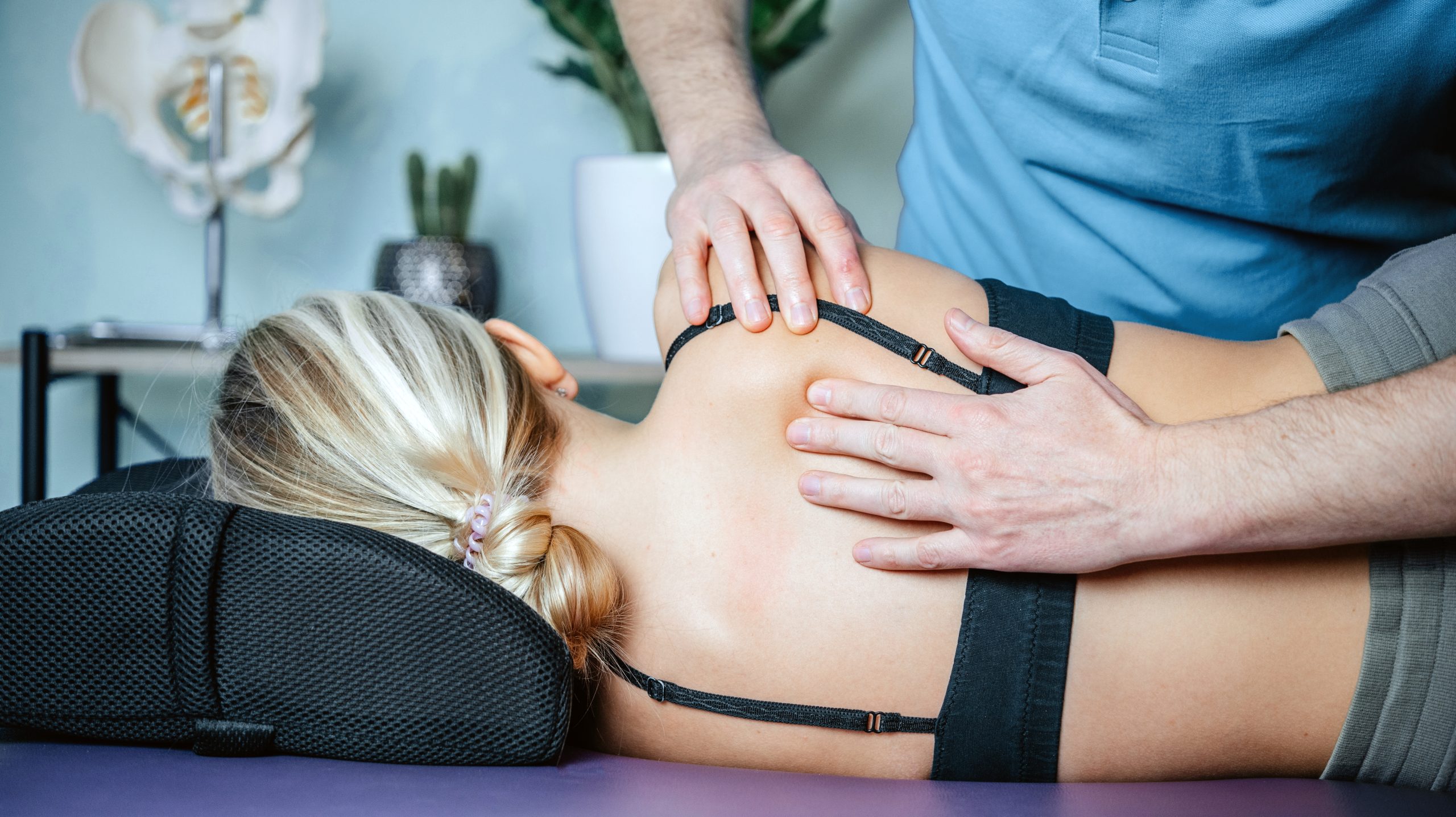 Een behandelaar masseert de schouder en bovenrug van een cliënt